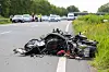 Zerstörtes Motorrad liegt auf der Landstraße, Einsatzkräfte und Fahrzeuge stehen im Hintergrund.