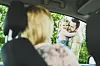 Frau im Auto blickt auf Mann mit Kind vor grüner Hecke; Abschiedsszene