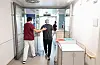 Pfleger begleitet Patienten im Flur des Klinikums Stuttgart, im Hintergrund weitere Beschäftigte.