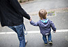 Erwachsene Person geht mit Kleinkind Hand in Hand auf einem Gehweg.