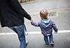 Erwachsene Person geht mit Kleinkind Hand in Hand auf einem Gehweg.