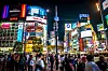Shibuya in Tokio bei Nacht mit leuchtenden Werbetafeln und dichtem Fußgängerverkehr.