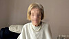 Frau sitzt auf dunklem Sofa in hellem Wohnraum mit Kissen im Hintergrund.