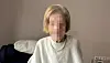 Frau sitzt auf dunklem Sofa in hellem Wohnraum mit Kissen im Hintergrund.