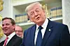 Donald Trump spricht im Oval Office, daneben zwei Männer im Anzug, Hintergrund mit Bücherregal.