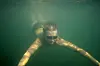 Person schwimmt mit Schwimmbrille unter Wasser im See.