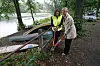 Zwei Personen sichern ein kleines Boot mit Seilen am Flussufer.