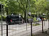 Schwarzer Transporter und weitere Autos auf nasser Straße unter grünen Bäumen.