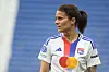 Dzsenifer Marozsán im weißen OL-Trikot vor blauem Stadionhintergrund.