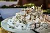 Weiße Schale mit Feta-Würfeln, mit Kräutern bestreut, auf hellem Tisch.
