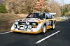 Audi Sport quattro S1 mit Zusatzscheinwerfern fährt schnell über kurvige Landstraße.