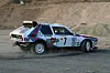 Weiß-blauer Lancia Delta S4 mit Martini-Streifen und Startnummer 7 auf Schotterpiste.