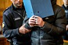 Beamter mit „Justiz“-Aufschrift führt verdeckte Person in Innenraum.