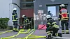 Feuerwehrkräfte mit Schläuchen und Ausrüstung vor einem Gebäudeeingang.