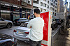 Mann lädt ein Elektroauto an einer Ladesäule am Straßenrand in der Stadt.