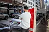 Mann lädt ein Elektroauto an einer Ladesäule am Straßenrand in der Stadt.