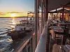 Blick auf Boote im Hafen bei Sonnenuntergang neben einem Restaurant mit Tischen und Stühlen.