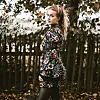 Frau im floralen Outfit steht im herbstlichen Park und blickt über die Schulter.