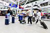 Reisende ziehen Koffer durch den Flughafen vor Check-in-Schaltern.