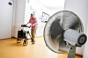 Frau mit Rollator im Flur eines Seniorenheims, im Vordergrund ein Ventilator.