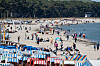 Touristen spazieren am Strand von Binz zwischen bunten Strandkörben und Badegästen.
