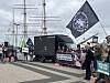 Demonstrierende mit Fahnen und Transparenten vor einem Segelschiff am Hafen, daneben ein schwarzer Lkw mit Bildschirm.