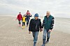 Drei Generationen spazieren am Strand, weitere Familienmitglieder folgen im Hintergrund.