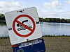 Badeverbotsschild am Ufer des Eichbaumsees in Hamburg bei blaugrünem Wasser und Sommerhimmel.