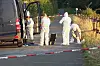 Beamte in Schutzanzügen untersuchen einen abgesperrten Straßenabschnitt neben einem Transporter.