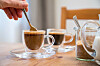 Frau rührt in einer Hamburger Wohnung Kaffee um, auf dem Tisch stehen Tassen und ein Zuckerglas.