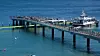 Langer Pier über blauem Meer mit Spaziergängern und einem Schiff am Ende.