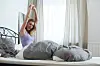 Frau streckt sich morgens im hellen Schlafzimmer im Bett.