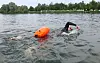 Schwimmer im Neoprenanzug im Schwarzachtalsee bei Ertingen, daneben eine orange Boje.