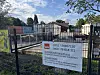 Bauzaun mit Schildern vor Baustelle an der Straße, dahinter Container und Bäume
