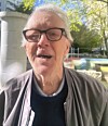Älterer Mann mit Brille vor Bäumen und Bank im Freien.