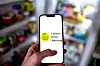 Hand hält Smartphone mit der App «Lebensmittelwarnung» vor geöffnetem Kühlschrank.
