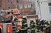 Feuerwehrleute arbeiten vor einem Gebäude mit Einsatzfahrzeug, Leitern und Ausrüstung.