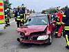 Rettungskräfte neben schwer beschädigtem rotem Auto nach Unfall auf der Straße.