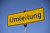 Gelbes Umleitungsschild auf Mast vor blauem Himmel