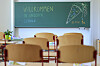 Leere Grundschule mit Tafel „Willkommen in unserer Schule“ und Stühlen im Klassenraum.