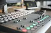 Audiomischpult mit beleuchteten Tasten in einem Studio vor Monitoren