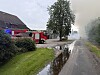 Feuerwehrfahrzeug neben Gebäude an verrauchter, nasser Straße mit Baum und Rauch im Hintergrund