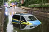 Polizeiwagen steht bis zur Tür im Hochwasser auf einer überfluteten Straße.