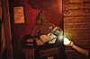 Goblin-artige Figur an einem Tresen mit Buch und Schild „Rezeption“, rot beleuchtete Fantasy-Szene.