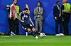 Lionel Messi spielt den Ball im dunkelblauen Argentinien-Trikot auf dem Rasen, im Hintergrund stehen Betreuer und Ordner.