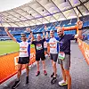 Vier Läufer stehen nach dem Zieleinlauf im Stadion nebeneinander und heben die Arme.