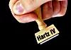 Eine Hand hält einen Stempel mit der Aufschrift „Hartz IV“.