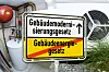 Ortsschild mit Gebäudemodernisierungsgesetz und durchgestrichenem Gebäudeenergiegesetz vor Gasheizung und Wärmepumpe.