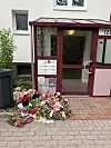 Blumen und Kränze liegen vor einem Hauseingang mit rotem Vordach.