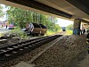 Entgleister Güterwagen neben Bahngleisen unter einer Brücke, im Hintergrund Einsatzkräfte und Zuschauer.